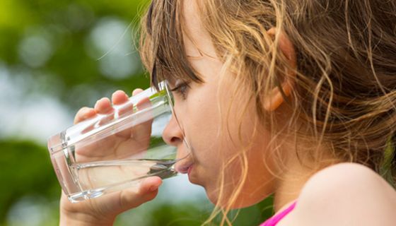 Nahaufnahme Gesicht Mädchen im Profil, nasse Haare, Ansatz Badeanzug, beim Wassertrinken aus Glas