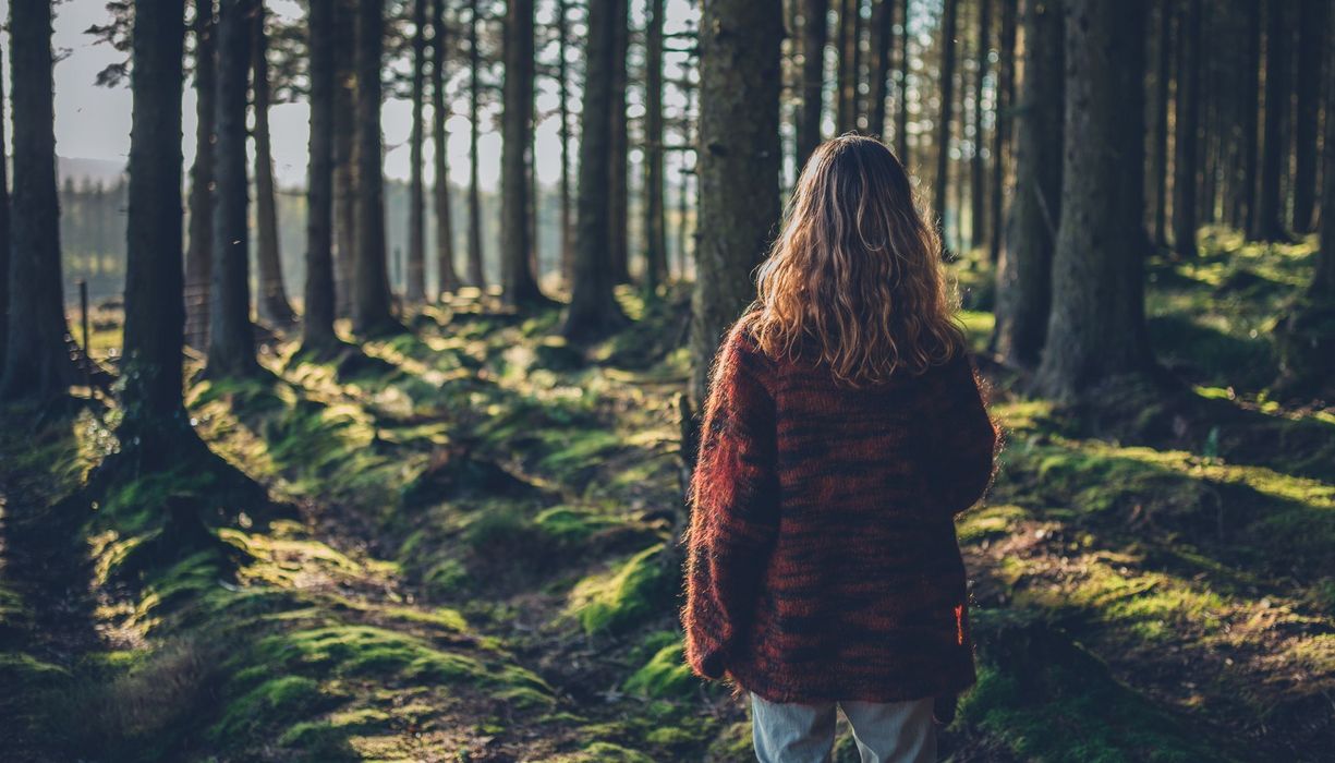 Junge Frau, steht im Wald, mit dem Rücken zur Kamera.