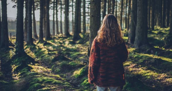 Junge Frau, steht im Wald, mit dem Rücken zur Kamera.