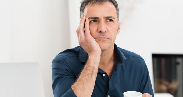 Mann mit Kaffeetasse schaut nachdenklich.