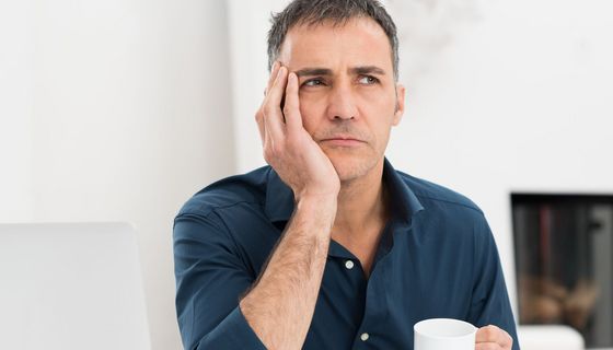 Mann mit Kaffeetasse schaut nachdenklich.