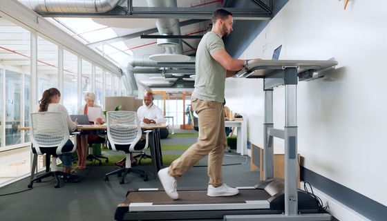 Junger Mann, läuft auf einem Laufband und arbeitet gleichzeitig am Laptop.