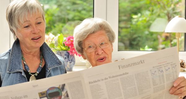 Zwei fröhliche alte Frauen lesen eine Tageszeitung