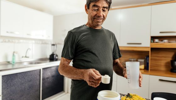 Ein älterer Mann misst mit einem Maßlöffel einen Eiweißshake ab.