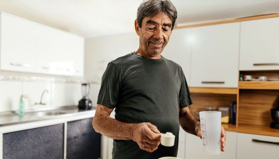 Ein älterer Mann misst mit einem Maßlöffel einen Eiweißshake ab.