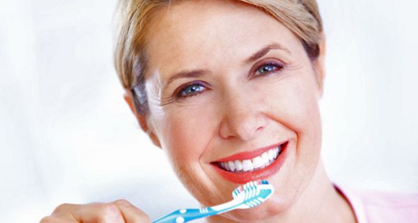 Mittelalte lachende Frau mit Zahnbürste vor dem Mund