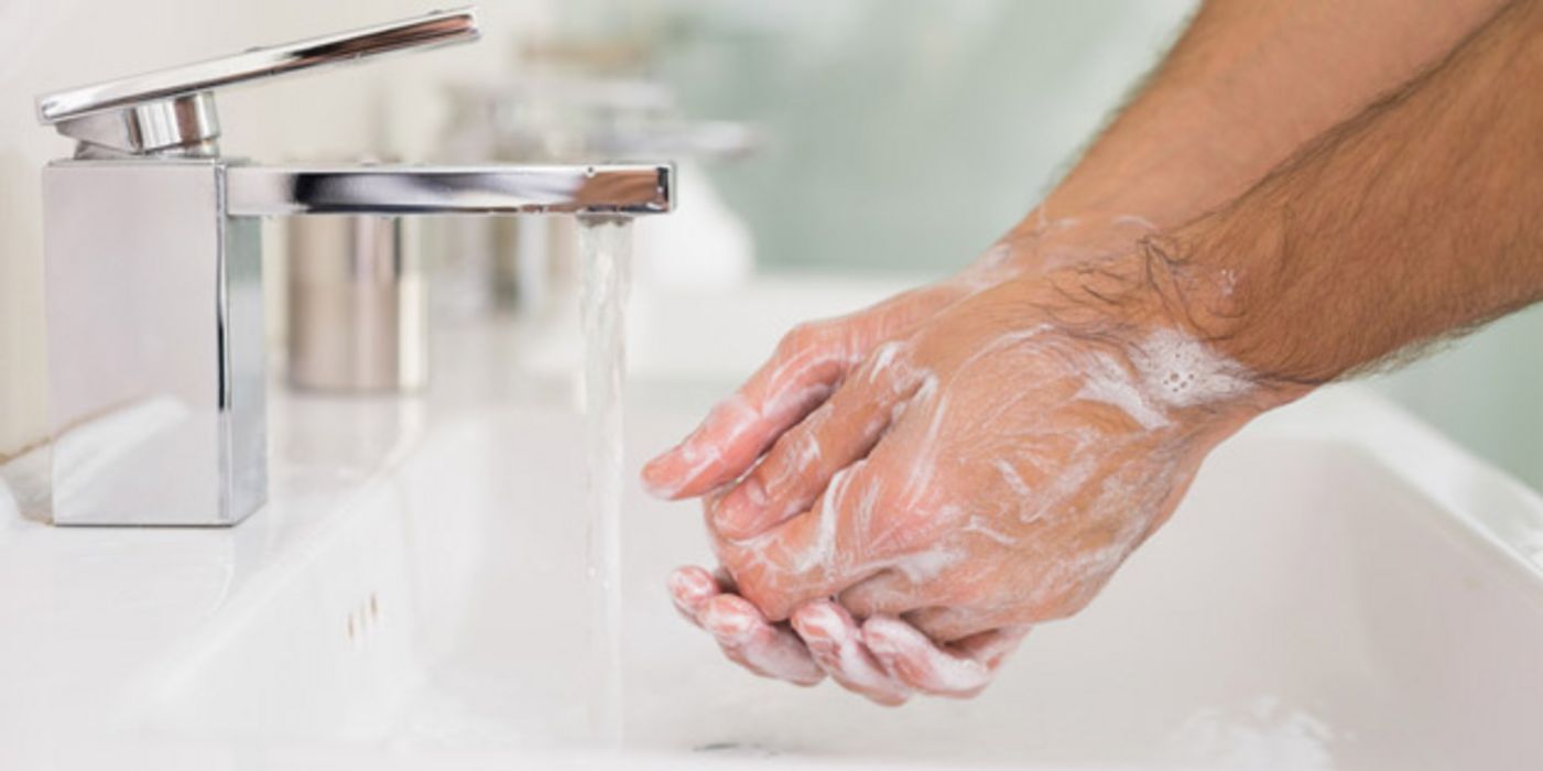 Eingeseifte Männerhände über Waschbecken unter fließendem Wasserhahn