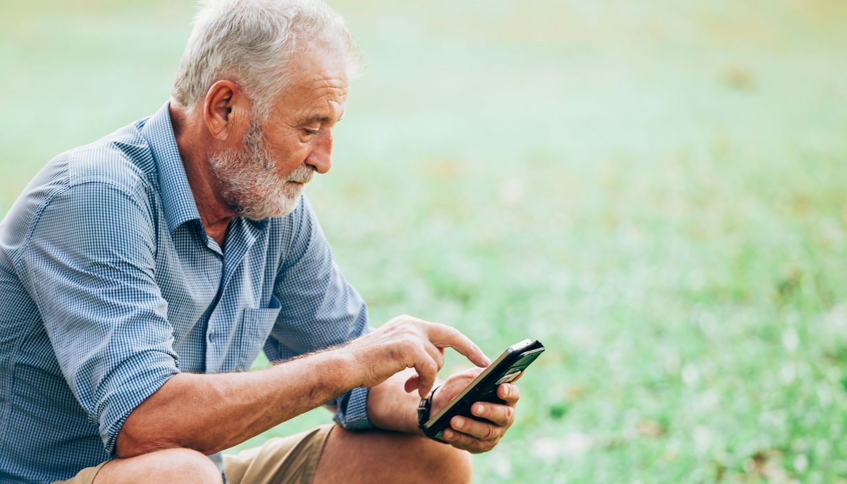 Älterer Mann, tippt auf Smartphone.