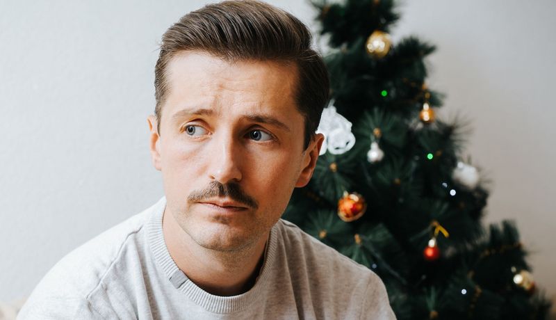 Ein Mann um die 40 sitzt vor einem kleinen Weihnachtsbaum und blickt traurig.