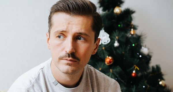 Ein Mann um die 40 sitzt vor einem kleinen Weihnachtsbaum und blickt traurig.