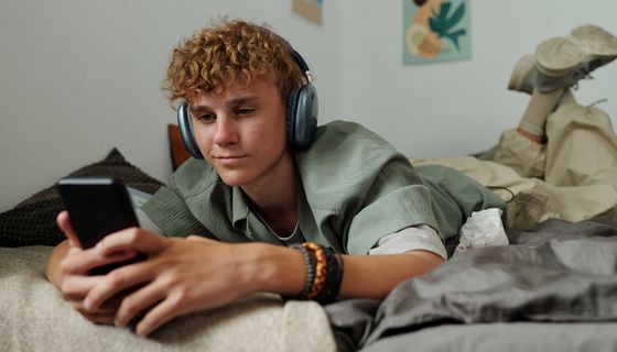 Ein Teenager liegt auf seinem Bett und schaut in sein Smartphone