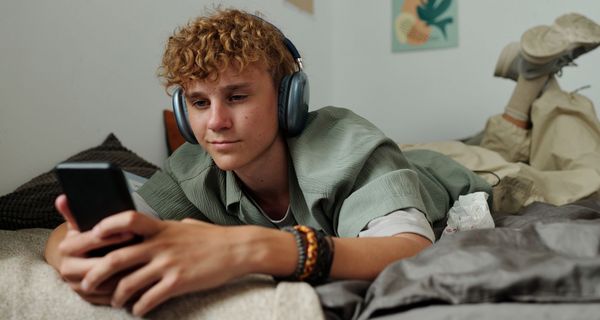 Ein Teenager liegt auf seinem Bett und schaut in sein Smartphone