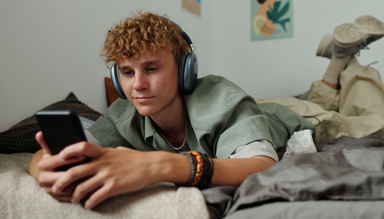 Ein Teenager liegt auf seinem Bett und schaut in sein Smartphone