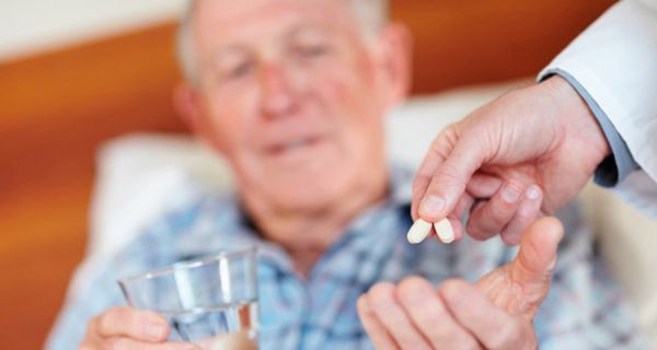 Alter Mann bekommt von einem Arzt zwei Tabletten in die Hand gedrückt