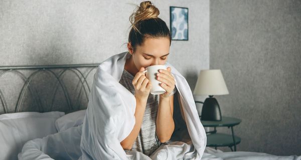 Junge Frau, sitzt im Bett und trinkt Kaffee.