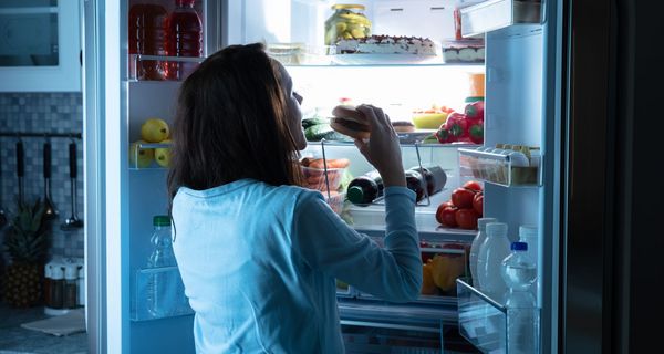 Frau, isst nachts einen Burger aus dem Kühlschrank.