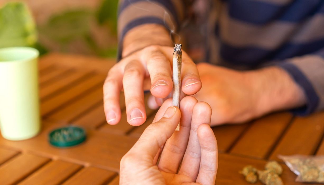 Mann, reicht seinem Gegenüber einen Joint.