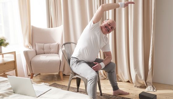 Älterer Herr macht Fitnessübungen auf einem Stuhl.