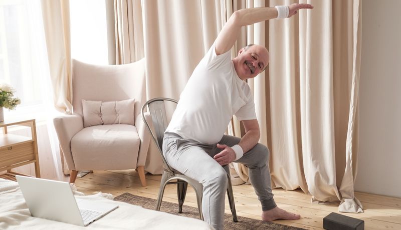 Älterer Herr macht Fitnessübungen auf einem Stuhl.