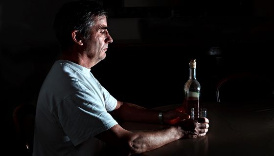 Älterer Mann, dunkler Hintergrund, trinkt Alkohol.