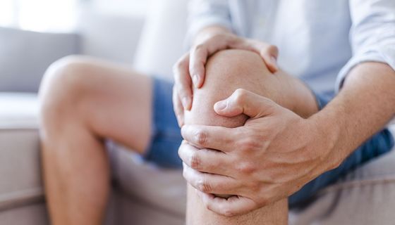 Mann, hält sich seine Hände am Knie.
