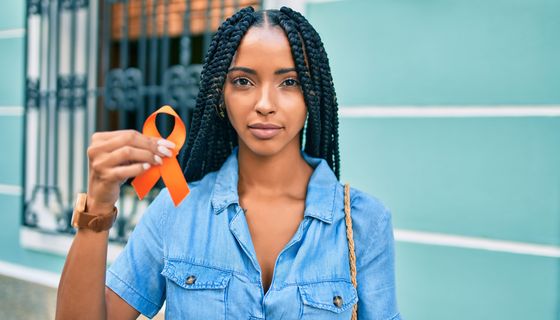 Junge Frau, hält eine orangefarbene Schleife in die Kamera.
