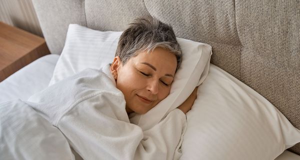 Frau mit kurzen, grauen Haaren schläft in einem Bett.