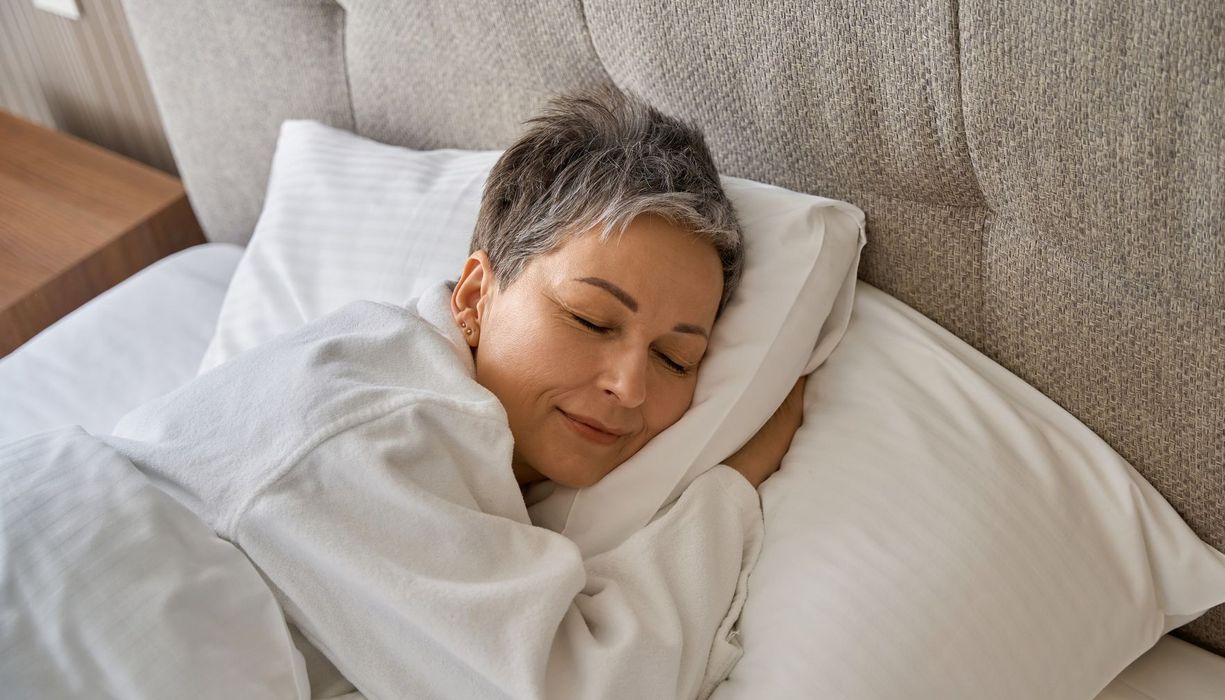 Frau mit kurzen, grauen Haaren schläft in einem Bett.