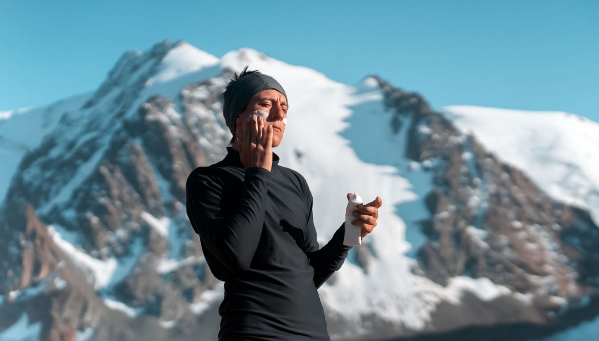 Mann steht vor Berg und cremt sein Gesicht mit Sonnencreme ein