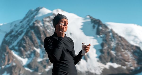 Mann steht vor Berg und cremt sein Gesicht mit Sonnencreme ein