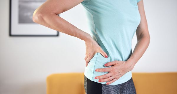 Eine Frau steht vor einem gelben Sofa und fasst sich an die Hüfte.