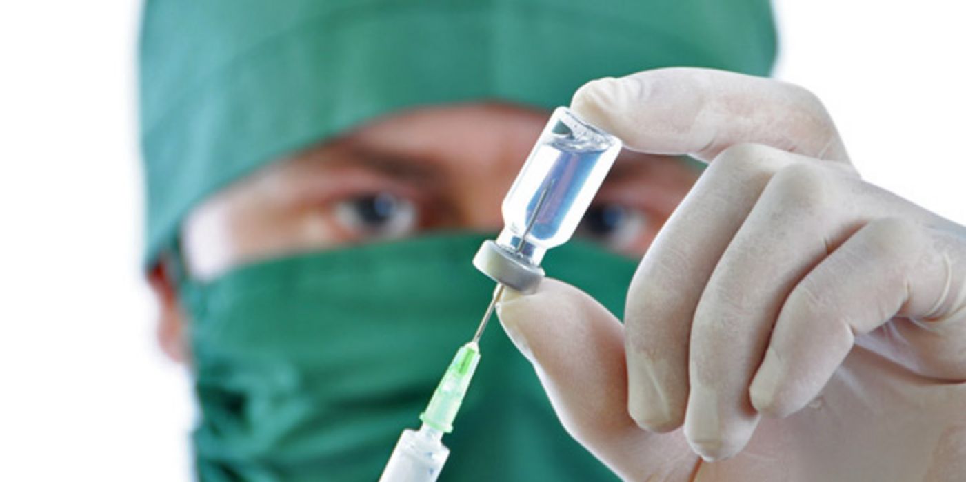 Arzt entnimmt mit einer Spritze Impfstoff aus einem Fläschchen
