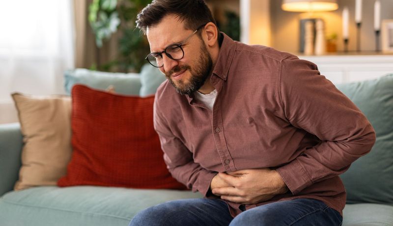 Mann hält sich den Bauch mit schmerzverzerrtem Gesicht.