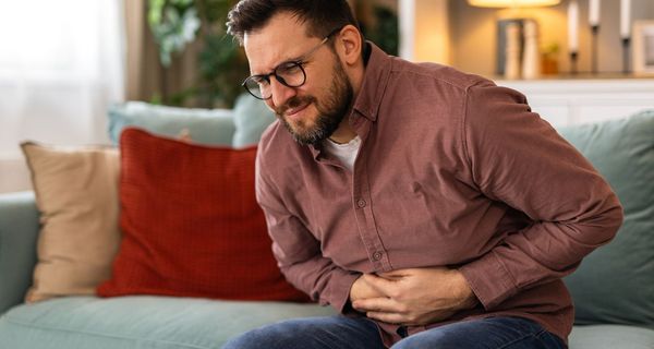 Mann hält sich den Bauch mit schmerzverzerrtem Gesicht.