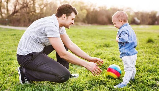 Vater spielt mit seinem Kleinkind auf einer Wiese Ball.