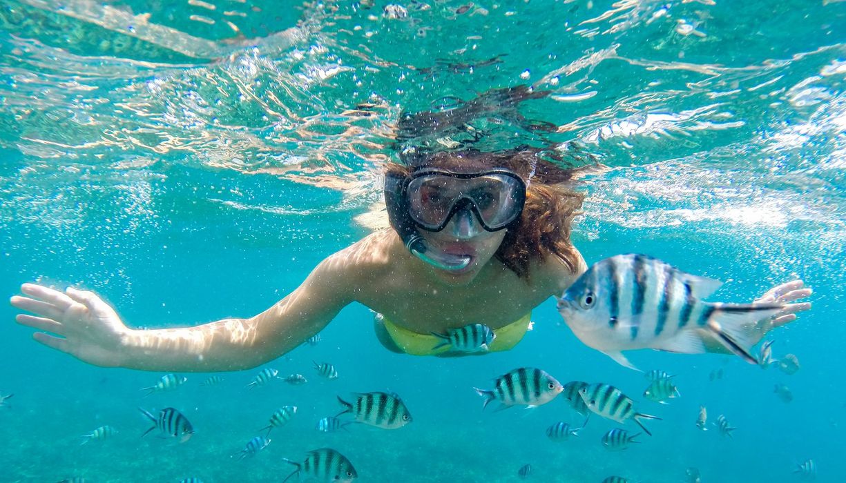Eine Frau schnorchelt mit einer Taucherbrille durch einen Fischschwarm.