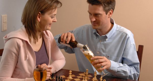Weintrinkende Frau und biertrinkener Mann spielen Schach