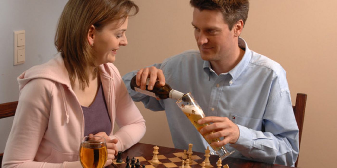 Weintrinkende Frau und biertrinkener Mann spielen Schach