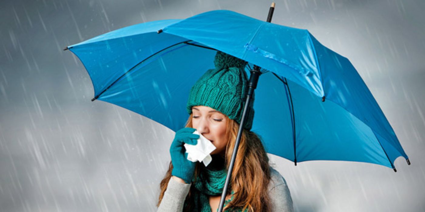 Frau unter türkisblauem Regenschirm putzt sich die Nase