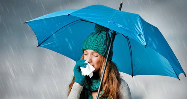 Frau unter türkisblauem Regenschirm putzt sich die Nase