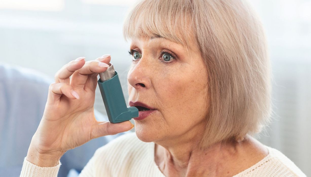 Ältere Frau inhaliert mit Asthma-Spray.