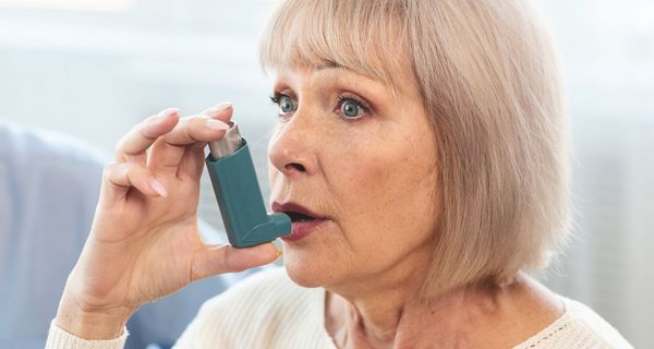 Ältere Frau inhaliert mit Asthma-Spray.