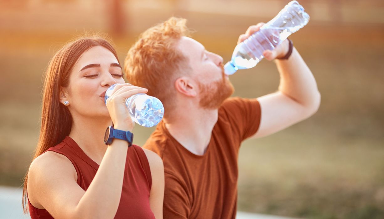 Junges sportliches Paar trinkt Wasser aus Plastikflaschen. 