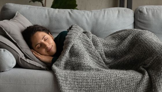 Eine Frau schläft bei Tag auf einem Sofa. Sie lächelt selig.
