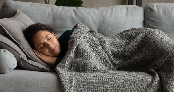 Eine Frau schläft bei Tag auf einem Sofa. Sie lächelt selig.