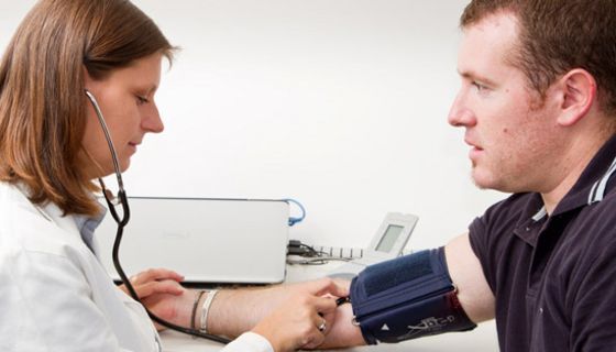 Ärztin, ca. 40, misst etwas korpulentem Patienten, ca. Mitte 30, den Blutdruck