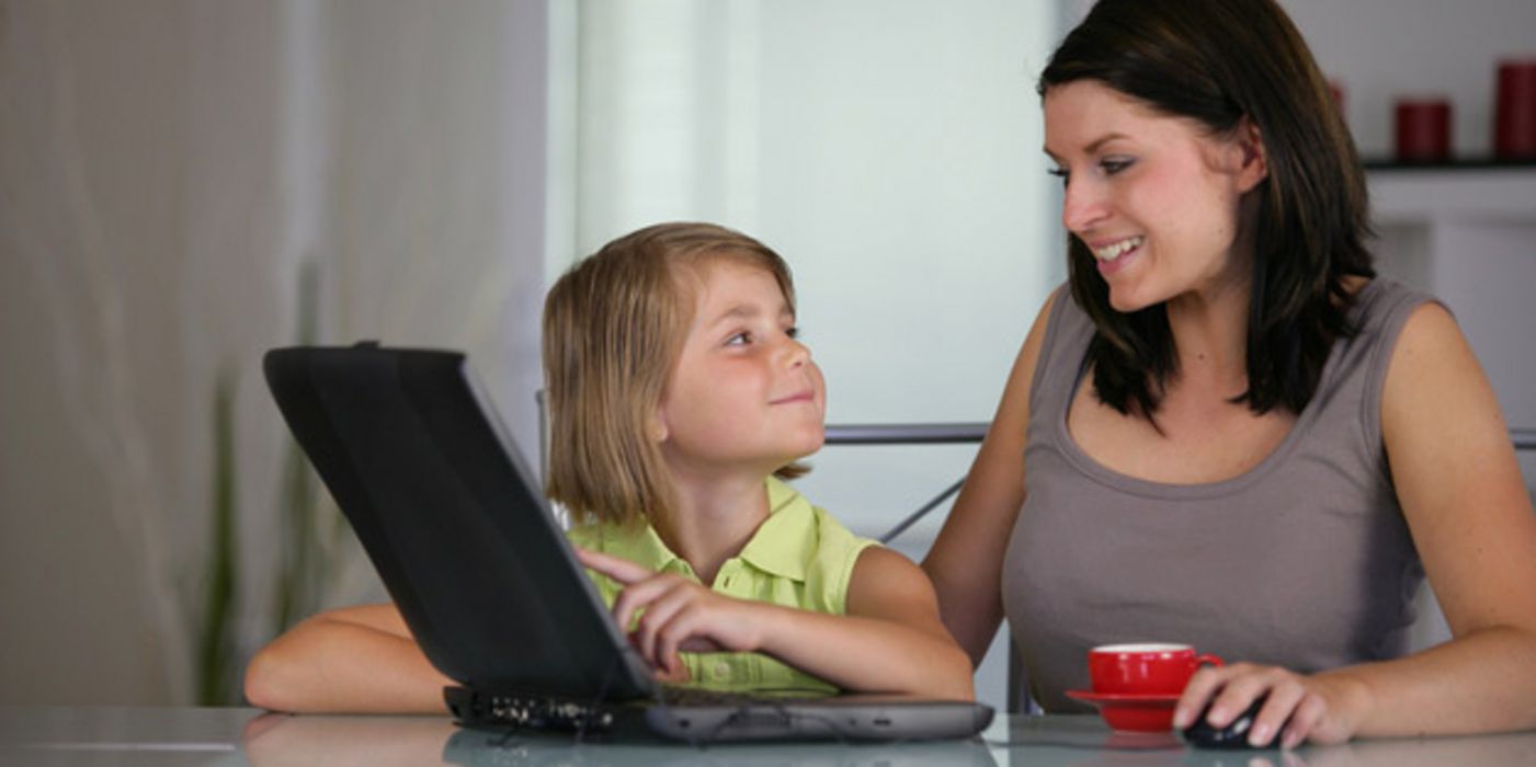 Ca. 9-jähriges, blondes Kind erklärt Mutter etwas am Laptop