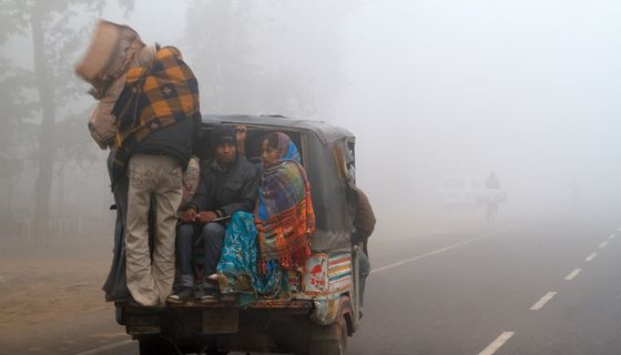 Eine indische Familie wird bei extrem rauen Wetterbedingungen in einer Auto-Rikscha transportiert. Neu-Delhi, eine landumschlossene, schnell wachsende Metropole mit mehr als 16 Millionen Einwohnern, ist in den Wintermonaten regelmäßig von Dunst und Smog (manchmal euphemistisch als Nebel bezeichnet) umhüllt, da sich Luftdruck und kühlere Luft mit Baustaub, Rauch von Kuhmistbränden und Autoabgasen vermischen, die dann tagelang über der Stadt schweben.