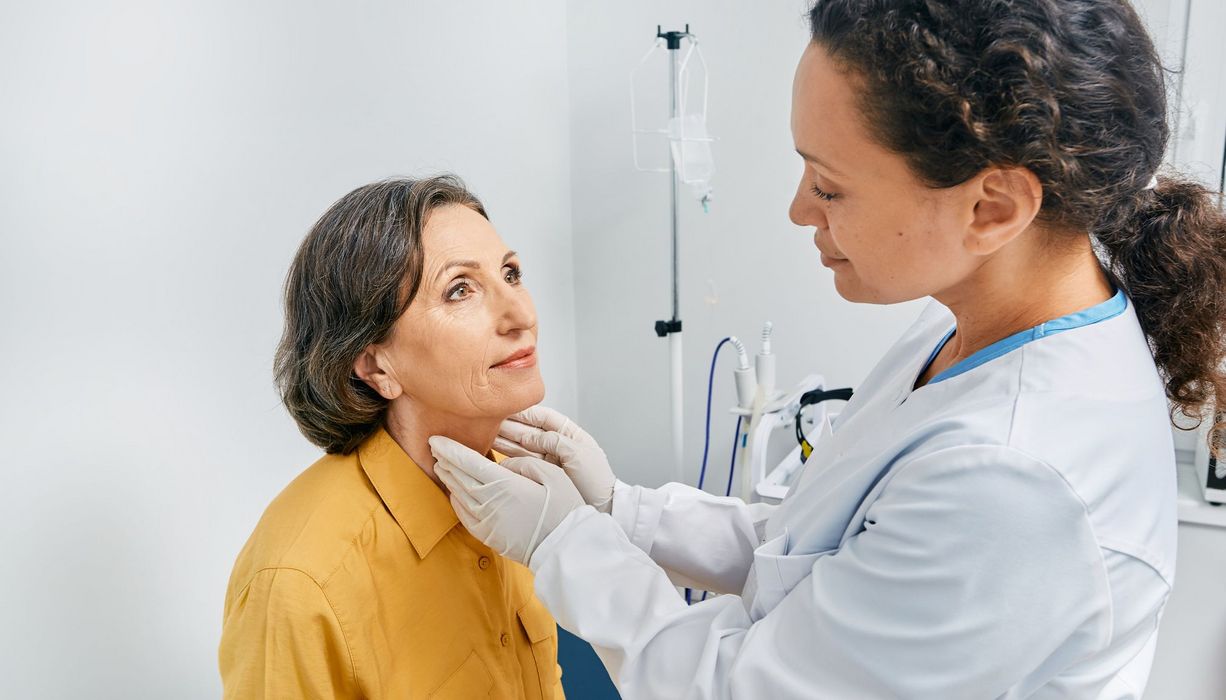 Ärztin, untersucht die Schilddrüse einer älteren Frau. 