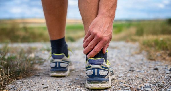 Mann, fasst sich beim Joggen an die Achillessehne.